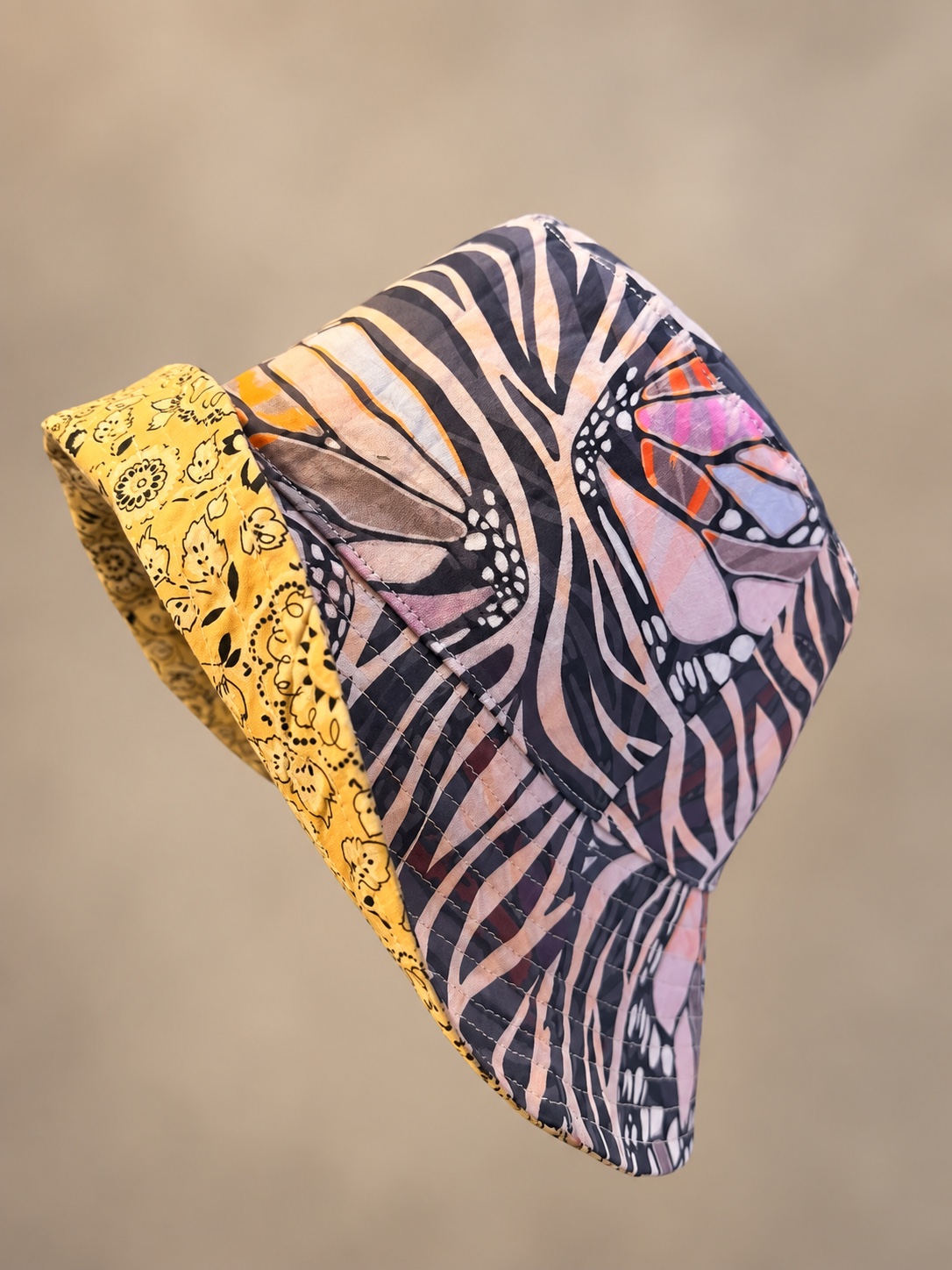 Butterfly-print bucket hat with black and pale pink wings, orange accents and a yellow floral lining