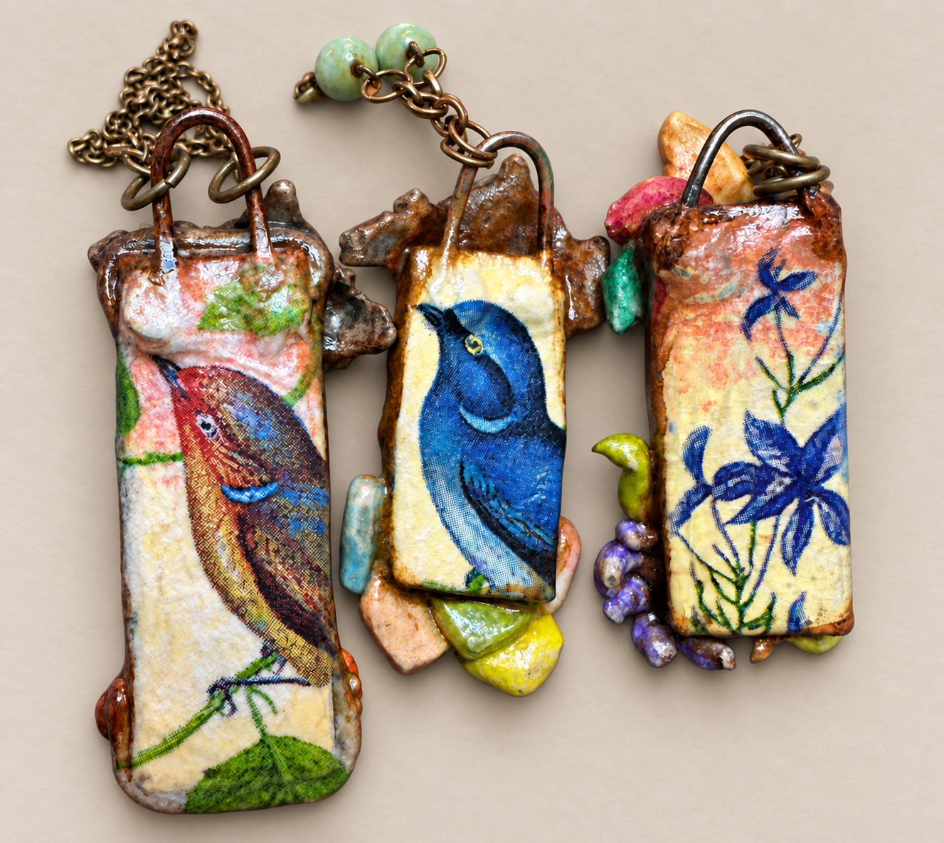 Reverse sides of three pendants showing colorful bird and floral artwork, resting on a warm neutral surface